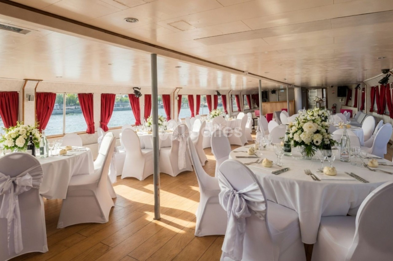 Salle de réception sur un bateau, décorée avec des tables rondes, nappes blanches, chaises ornées et grandes fenêtres avec…