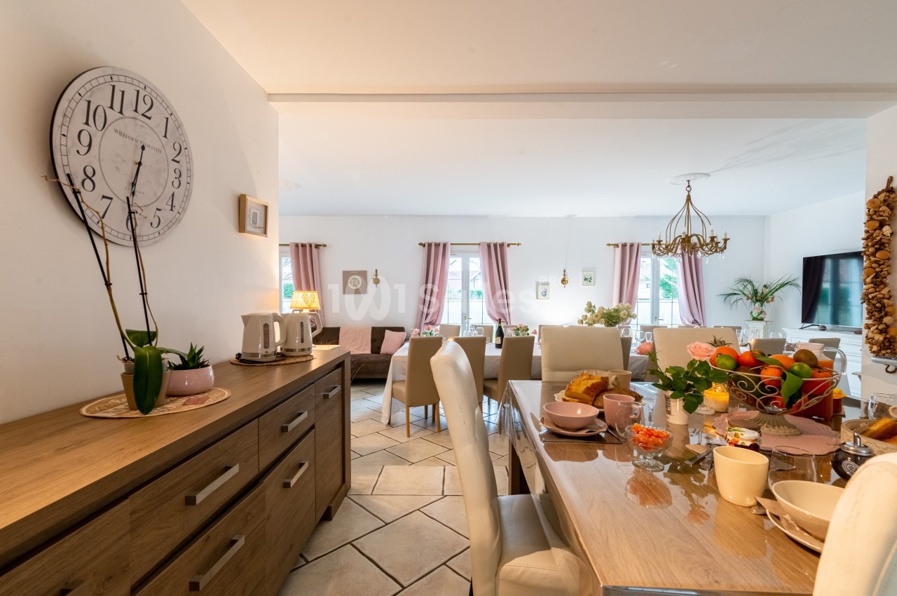 Salle à manger lumineuse avec table dressée, chaises blanches, buffet en bois et décoration chaleureuse.