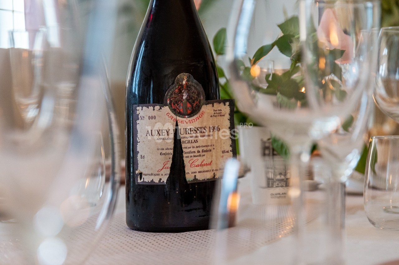 Bouteille de vin Auxey-Duresses 1996 posée sur une table dressée avec des verres et des décorations végétales.