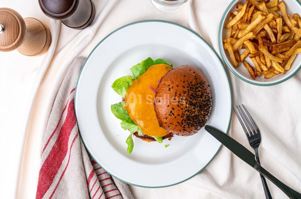 Burger au cheddar et salade servi dans une assiette blanche, accompagné de frites et d'ustensiles sur une nappe claire.