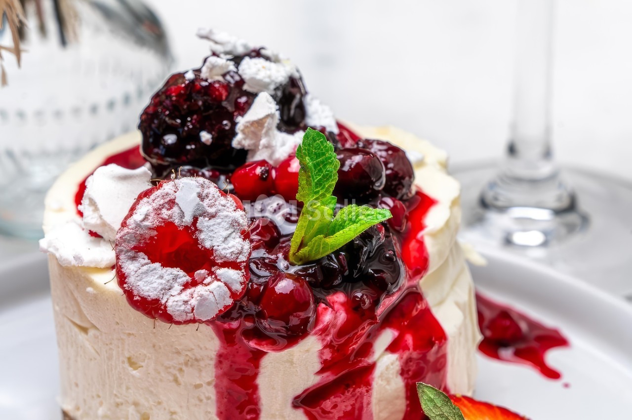 Gâteau au fromage garni de fruits rouges, coulis, menthe fraîche et éclats de meringue, présenté sur une assiette blanche.