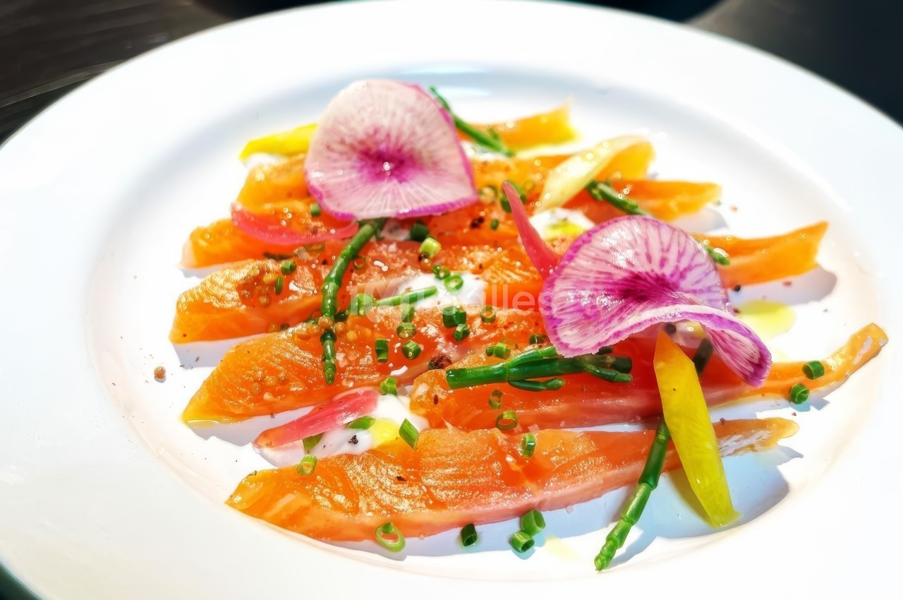 Tranches de saumon fumé garnies de radis roses, ciboulette et légumes colorés sur une assiette blanche.