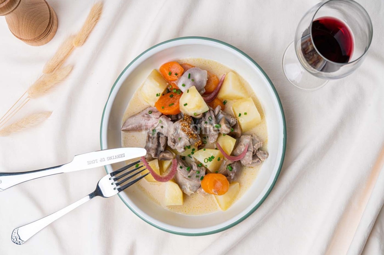 Assiette de blanquette de veau avec légumes, servie sur une nappe blanche, accompagnée d'un verre de vin rouge.