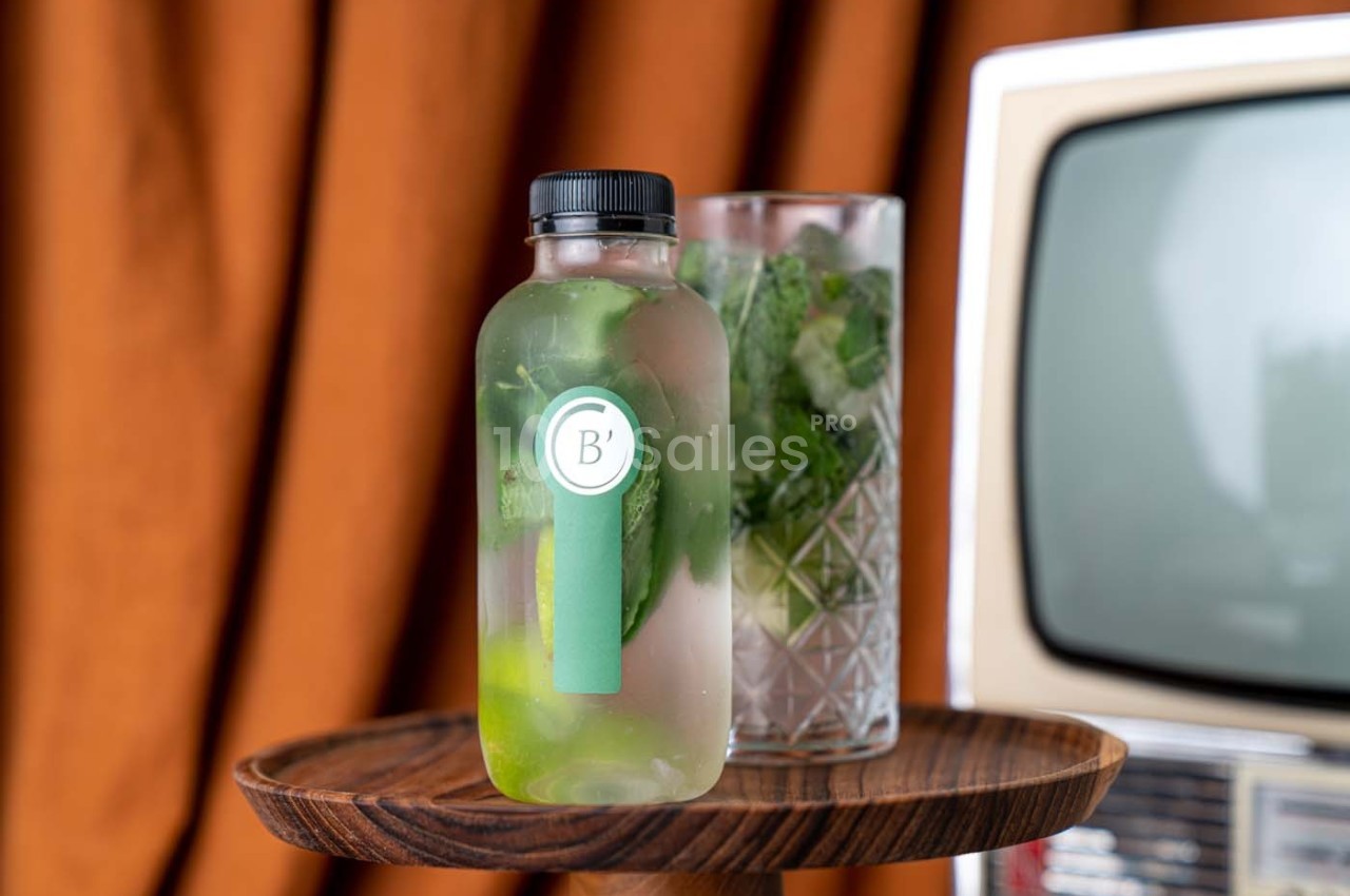 Bouteille en verre remplie d'eau infusée aux herbes et citron, posée sur un plateau en bois devant un verre et une…
