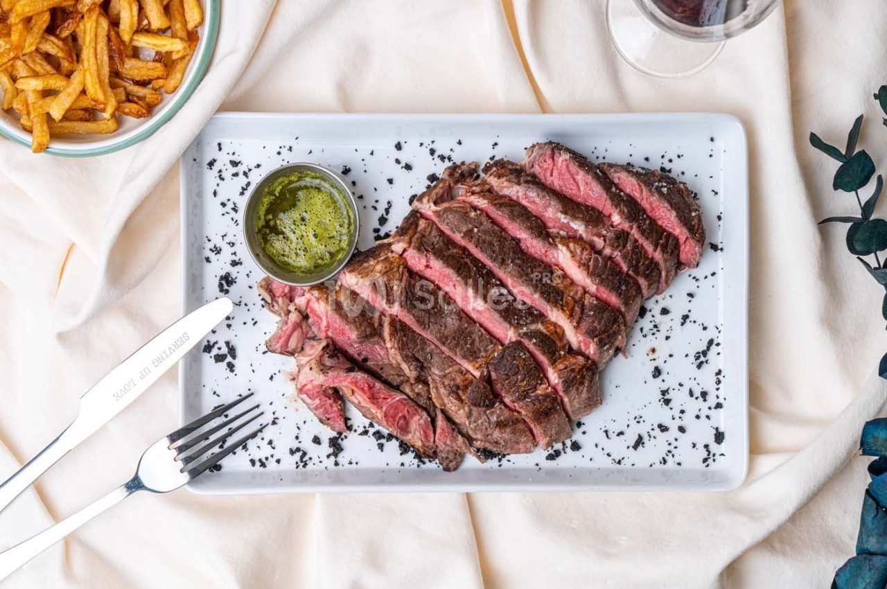 Assiette de viande de bœuf tranchée, accompagnée de sauce verte, frites et verre de vin rouge.