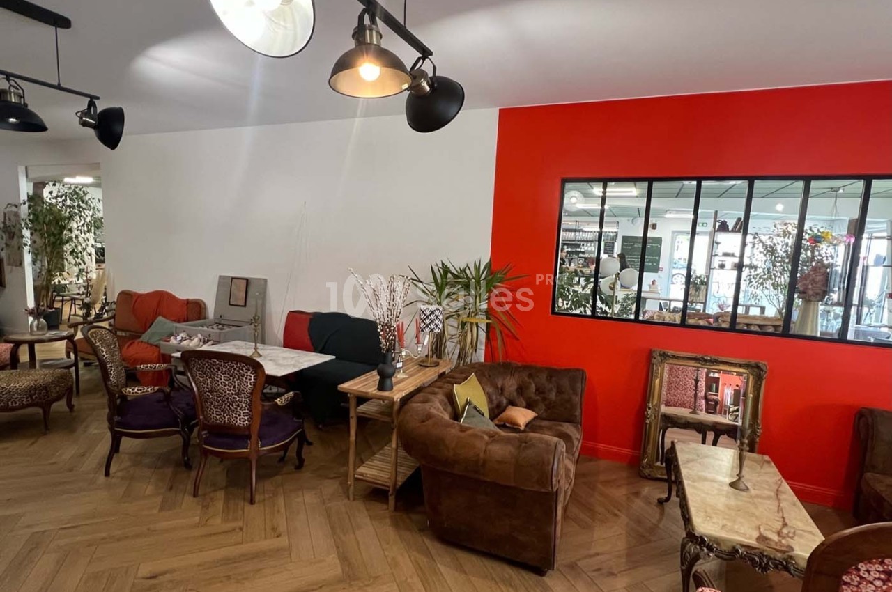 Espace intérieur chaleureux avec mobilier éclectique, murs blancs et rouges, et grande verrière donnant sur une autre pièce.