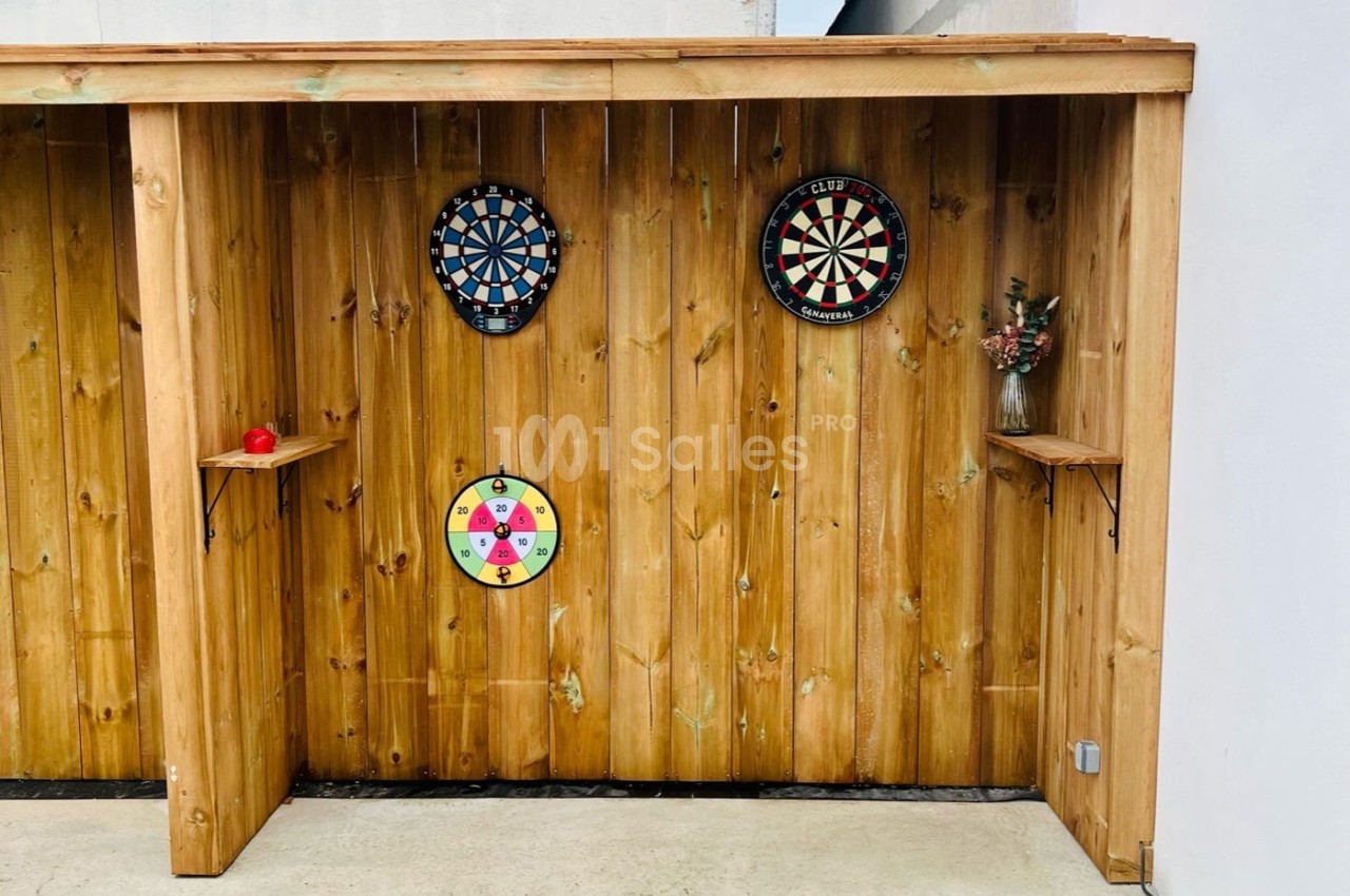 Trois cibles de fléchettes fixées sur une cloison en bois, avec une étagère contenant un vase et une pomme.