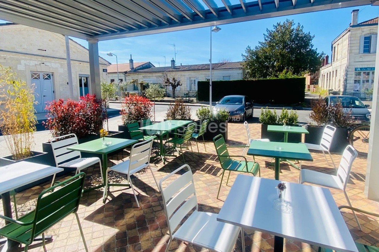 Terrasse extérieure avec tables et chaises vertes et blanches, entourée de plantes, sous un ciel bleu clair.