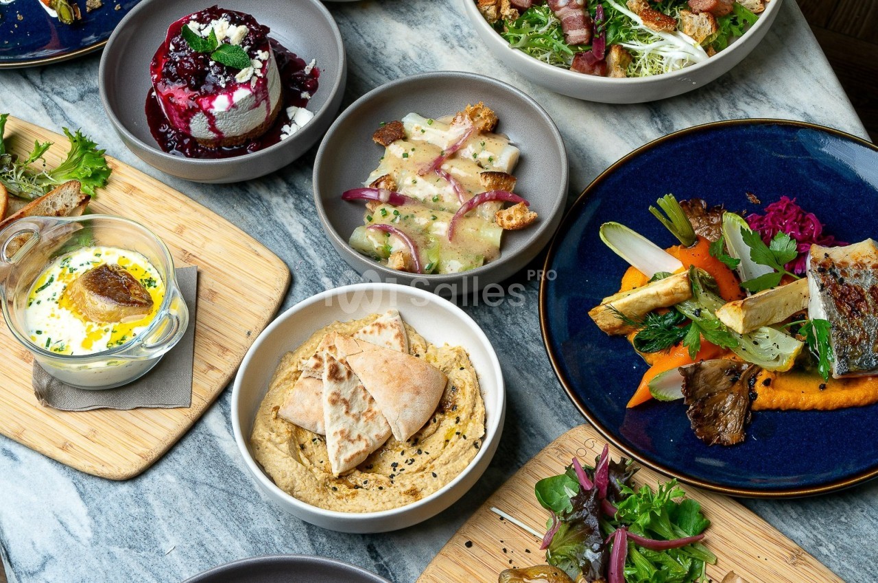 Assortiment de plats variés comprenant légumes, houmous, poisson grillé et desserts, disposés sur une table en marbre.