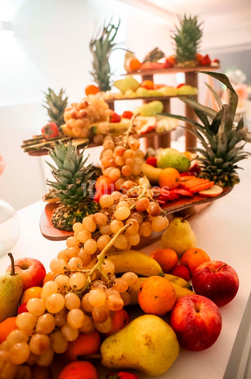 Plateau de fruits variés comprenant raisins, pommes, poires, ananas et agrumes disposés sur plusieurs niveaux.
