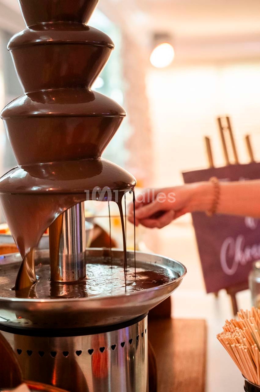 Fontaine de chocolat en fonctionnement avec une main tendue vers le flux, entourée d'ustensiles pour tremper.