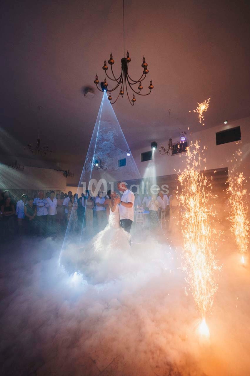 Un couple danse au centre d'une salle éclairée par des projecteurs, entouré de fumée et de jets d'étincelles.