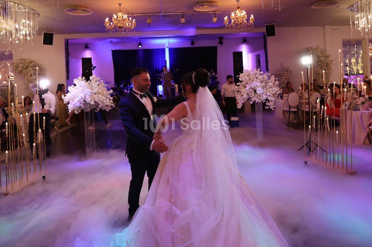 Un couple danse leur première danse de mariage dans une salle décorée avec des lumières et des fleurs, entouré de fumée au…