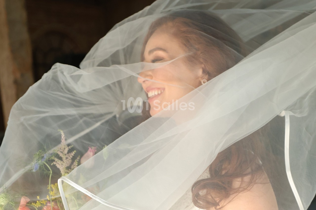 Femme souriante portant un voile de mariée translucide, tenant un bouquet de fleurs colorées.