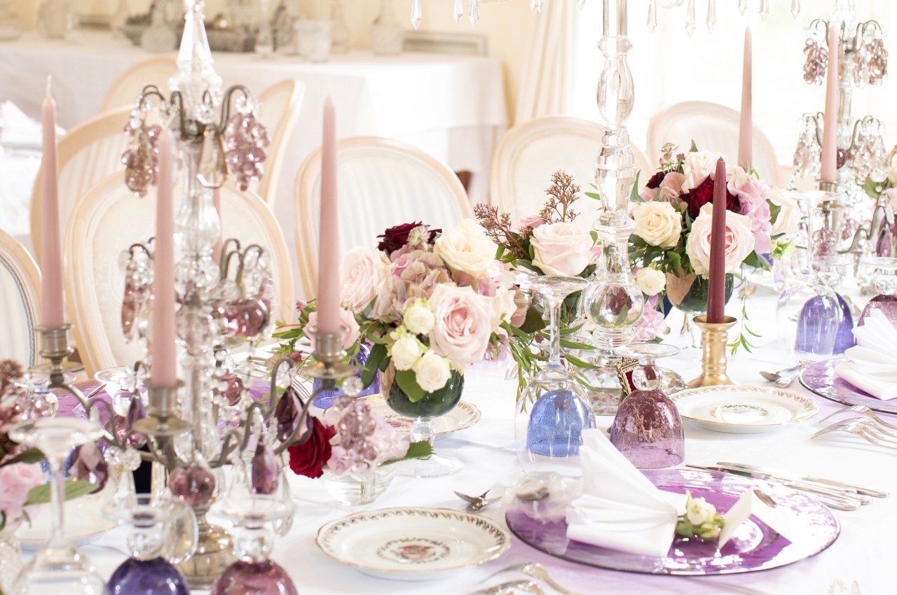 Table élégamment dressée avec chandeliers, fleurs pastel, assiettes décoratives et serviettes pliées.