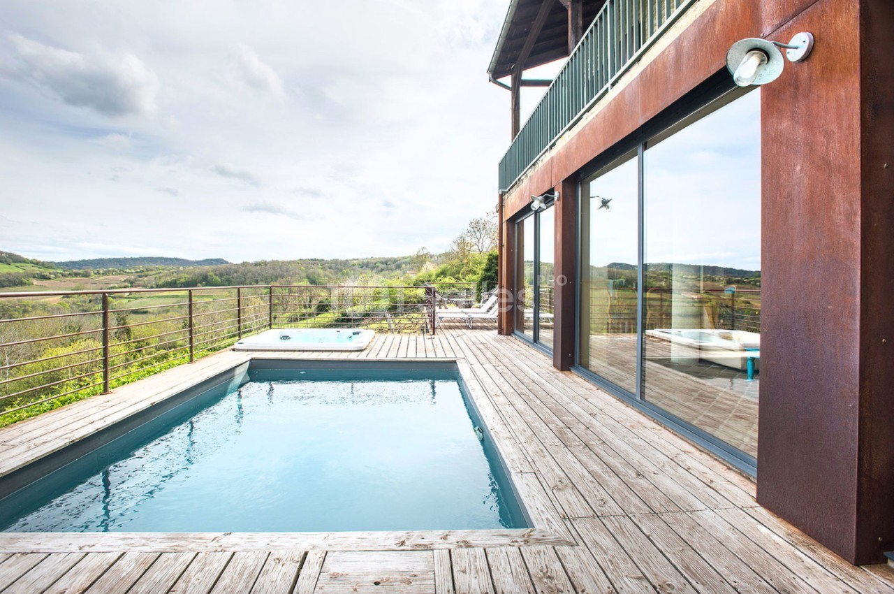 Piscine extérieure rectangulaire sur une terrasse en bois avec vue sur la campagne environnante.