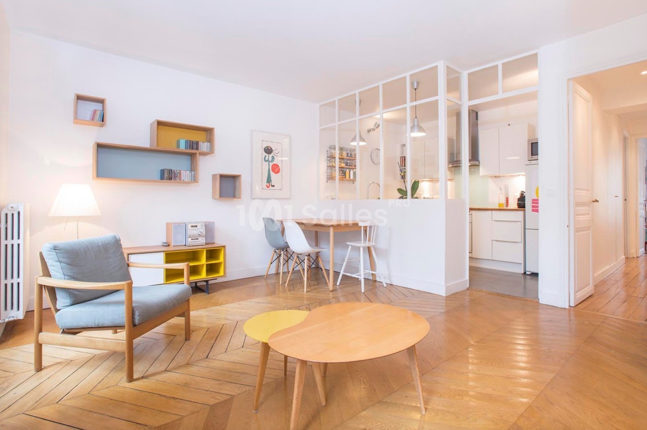 Salon lumineux avec parquet en bois, mobilier moderne, table à manger, et verrière séparant la cuisine.