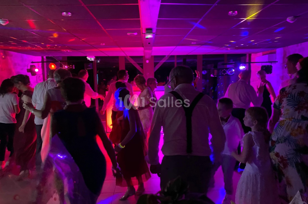 Des personnes dansent dans une salle éclairée par des lumières colorées lors d'une fête ou d'un événement.