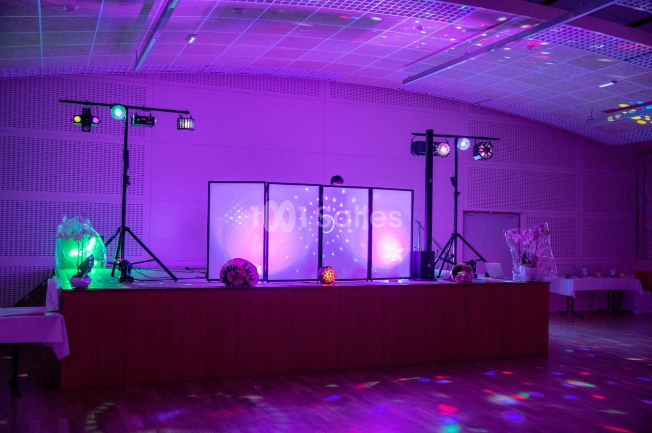 Scène de fête éclairée par des lumières colorées avec une table en bois et des équipements de sonorisation.