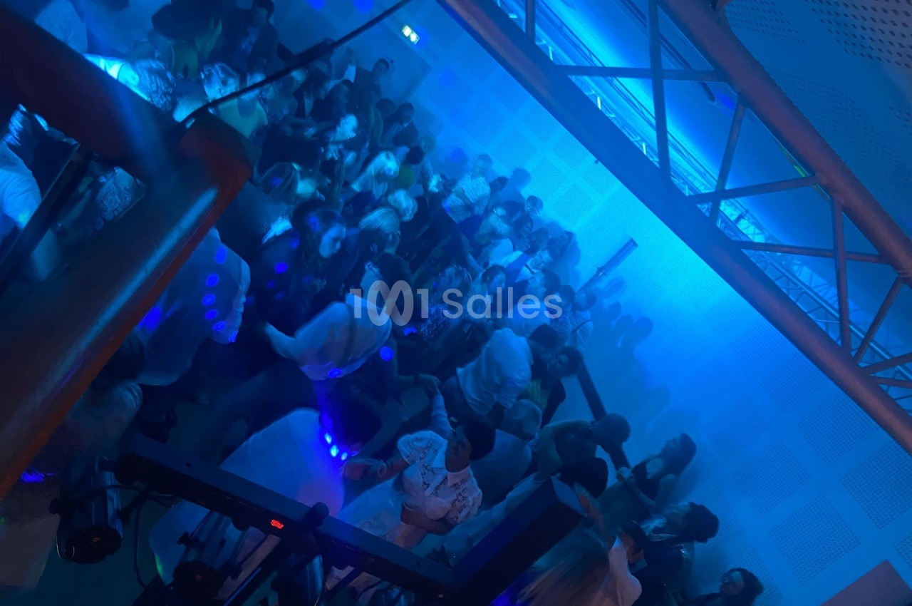 Groupe de personnes dansant dans une salle éclairée par des lumières bleues, ambiance festive et animée.