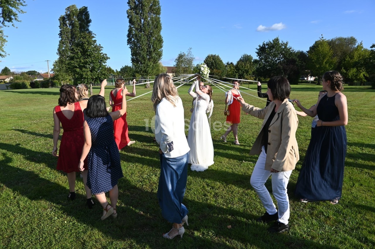 Des personnes dans un parc participent à une danse traditionnelle autour de rubans attachés à un bouquet.