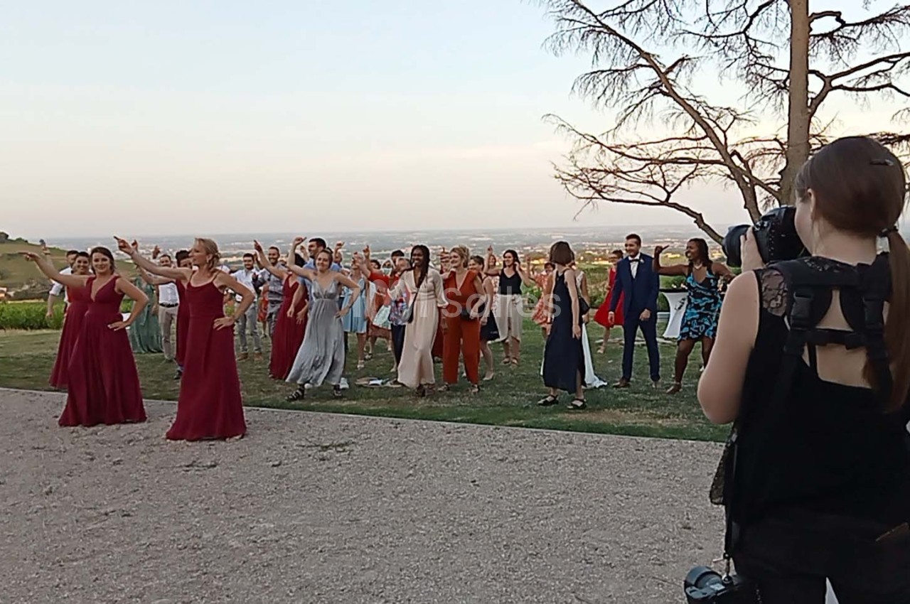Un groupe de personnes dansant en extérieur, photographié par une femme avec un appareil photo.