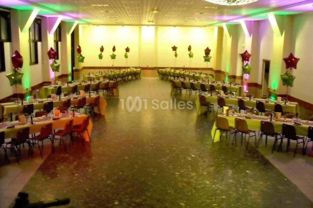 Salle de réception décorée avec des tables alignées, nappes colorées et ballons étoilés suspendus.