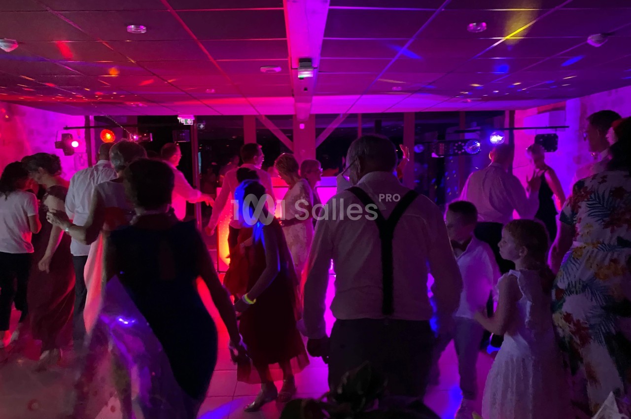 Des personnes dansent dans une salle éclairée par des lumières colorées lors d'une fête ou d'un événement.