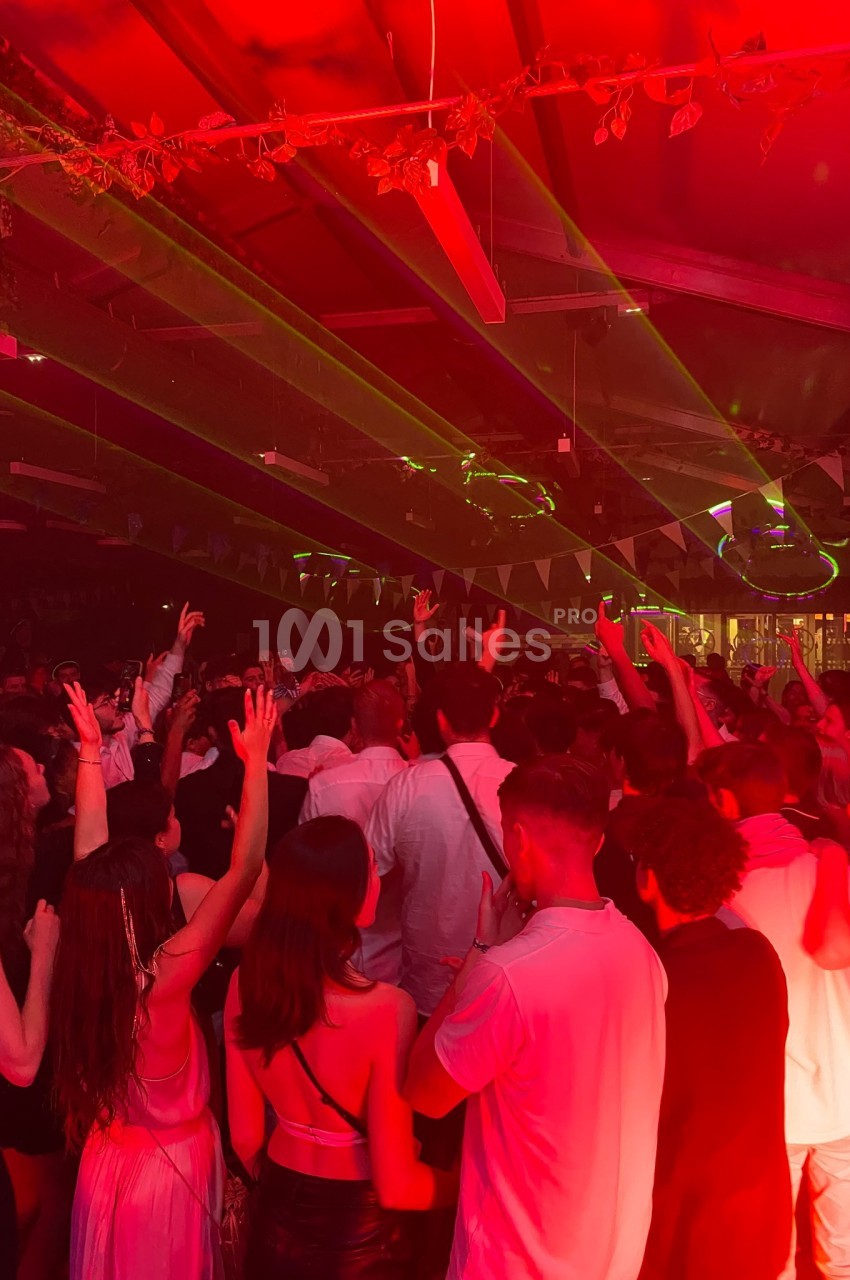 Foule dansante sous des lumières rouges et des lasers dans une ambiance festive en intérieur.