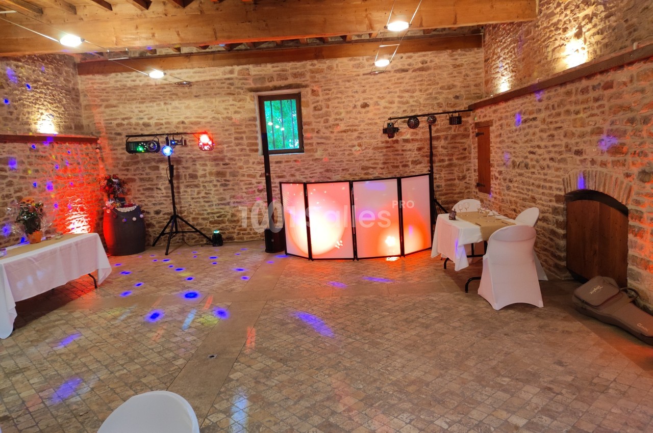 Salle en pierre avec éclairage coloré, tables décorées et espace aménagé pour une animation musicale.