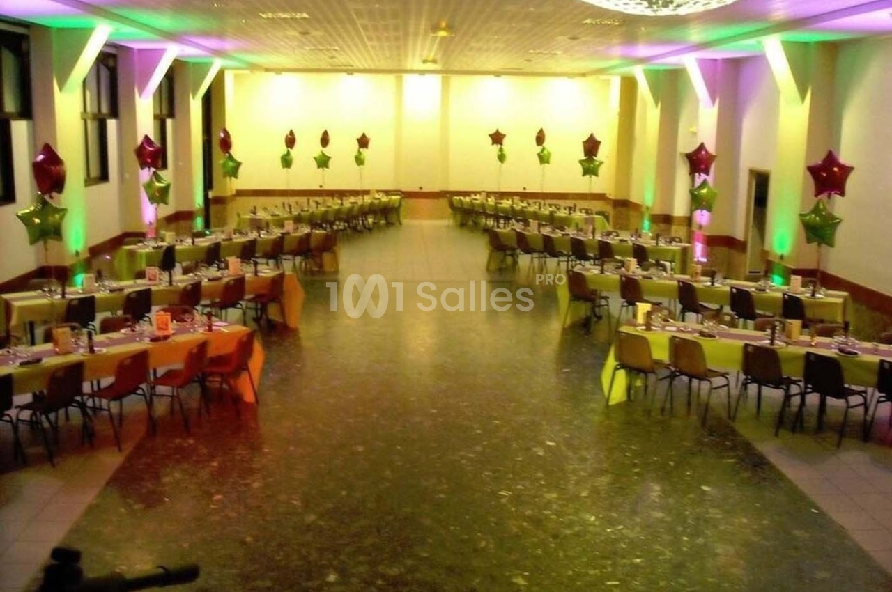 Salle de réception décorée avec des tables alignées, nappes colorées et ballons étoilés suspendus.