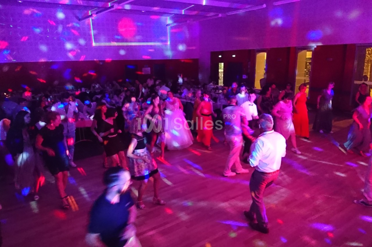 Des personnes dansent dans une salle éclairée par des lumières colorées lors d'une fête ou d'un événement.