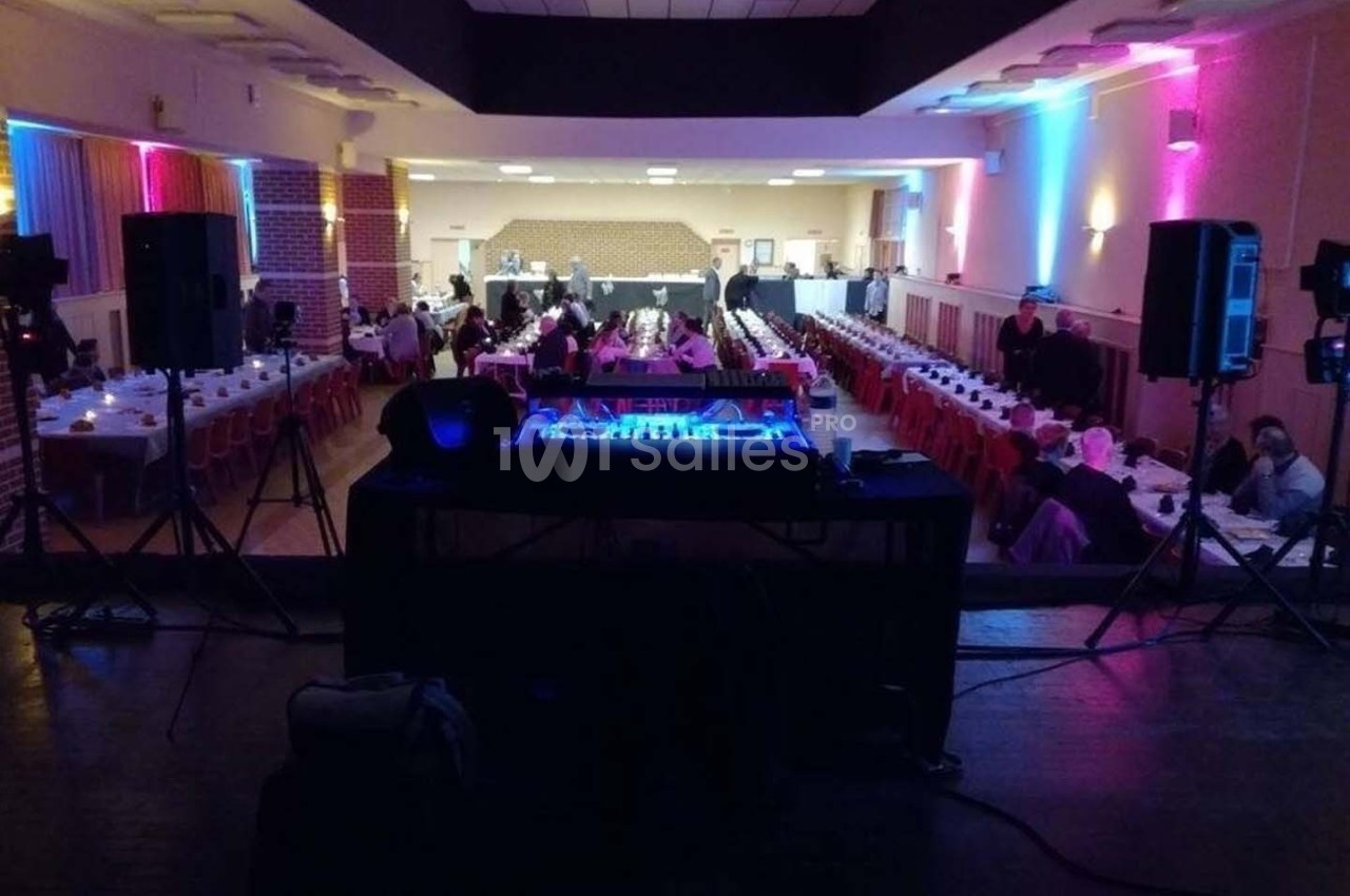 Salle de réception avec tables dressées, vue depuis une scène équipée d'une console de mixage lumineuse.
