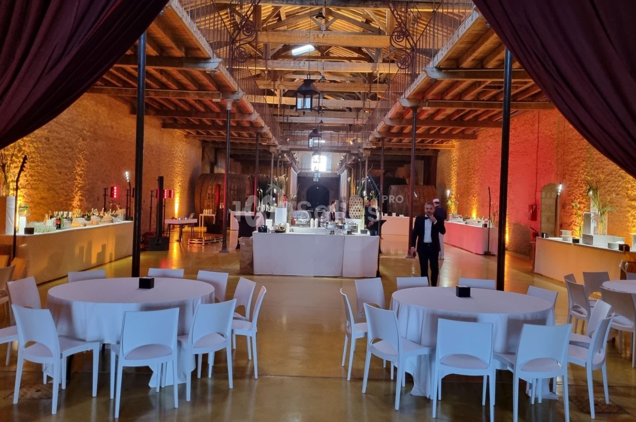 Salle de réception avec tables rondes dressées, éclairage chaleureux et buffets alignés le long des murs en pierre.