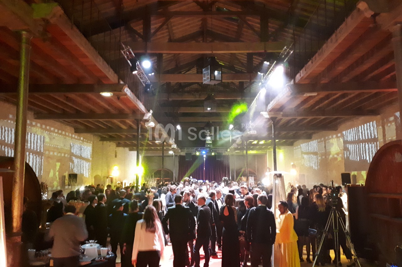 Salle spacieuse avec plafond en bois, éclairages colorés et foule rassemblée lors d'un événement festif.