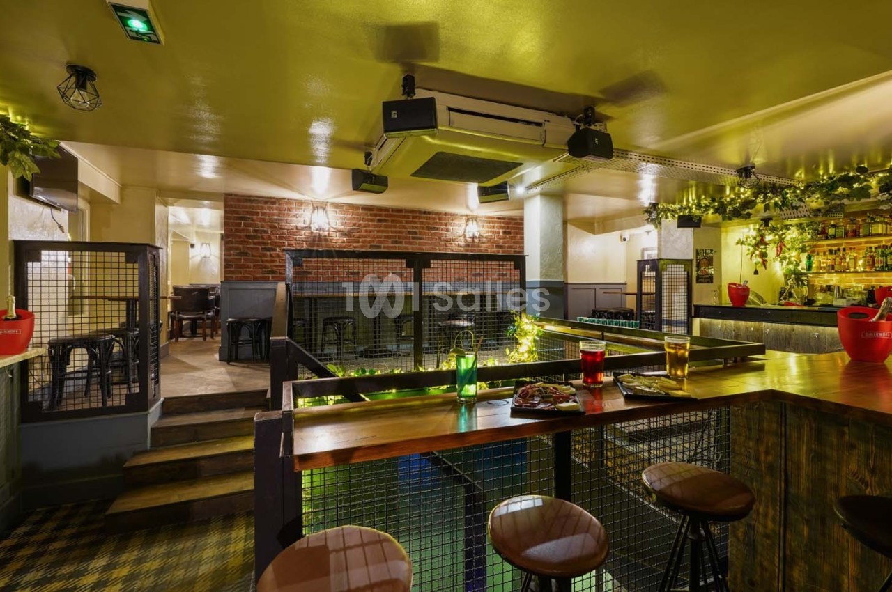 Intérieur d'un bar chaleureux avec comptoir en bois, tabourets, éclairage tamisé et décorations végétales.