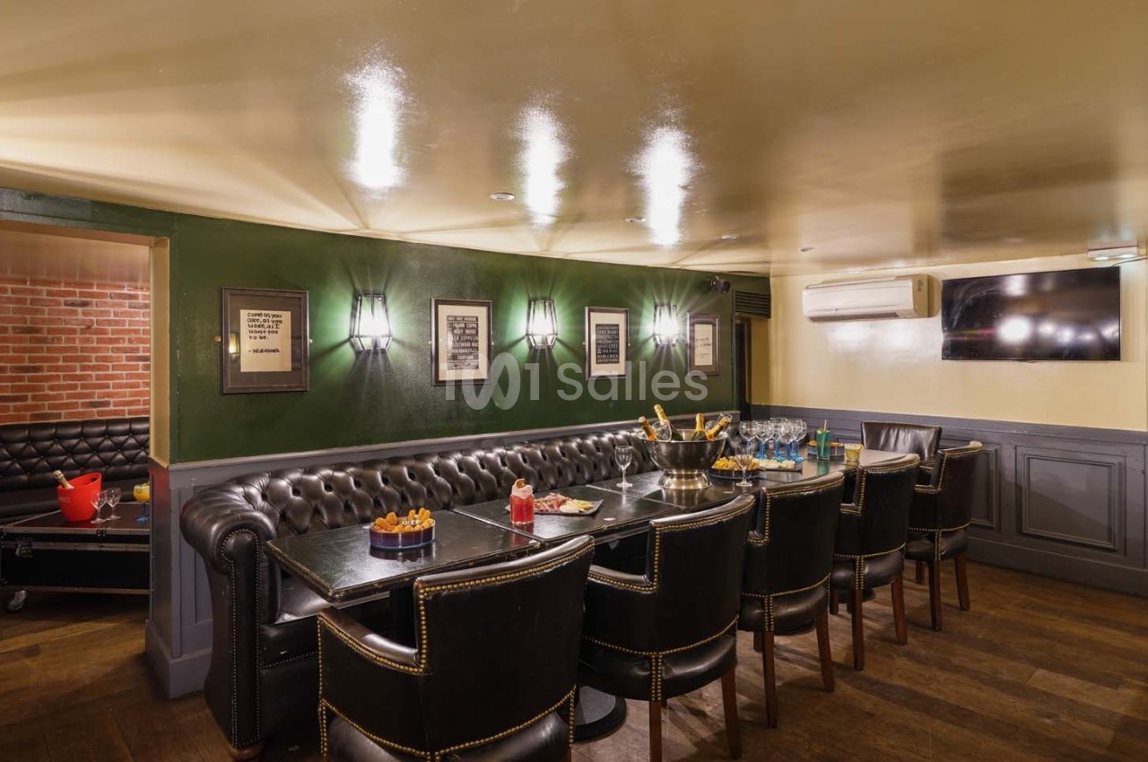 Salle à manger avec table rectangulaire, chaises en cuir, murs verts décorés de cadres et éclairage mural.