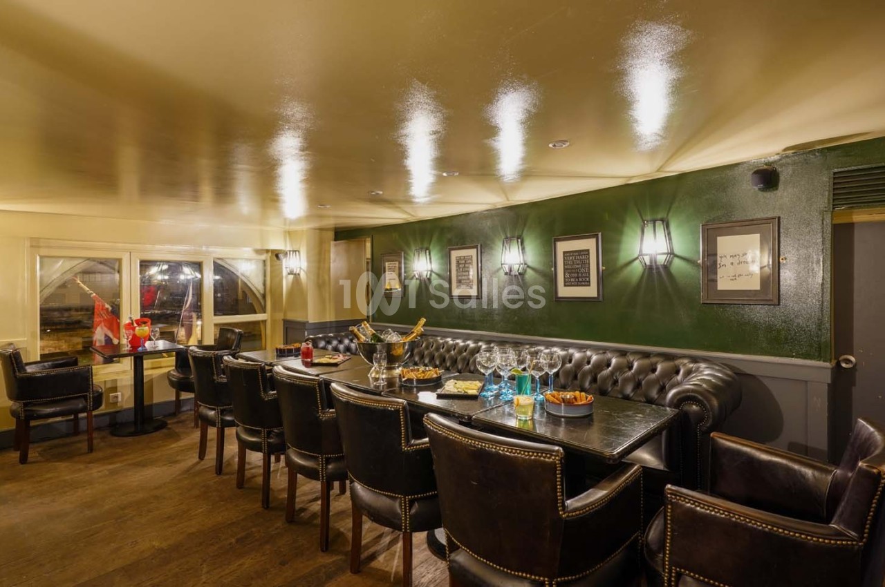 Salle élégante avec table en bois, chaises en cuir, murs verts, éclairage tamisé et vue sur l'extérieur.