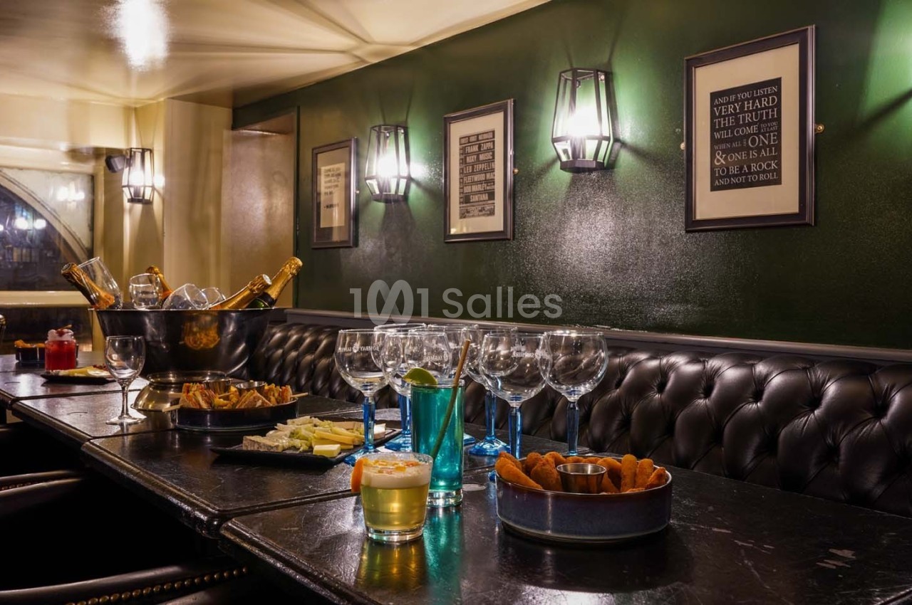 Salle avec banquettes en cuir, table dressée avec verres, bouteilles, amuse-bouches et éclairage mural tamisé.
