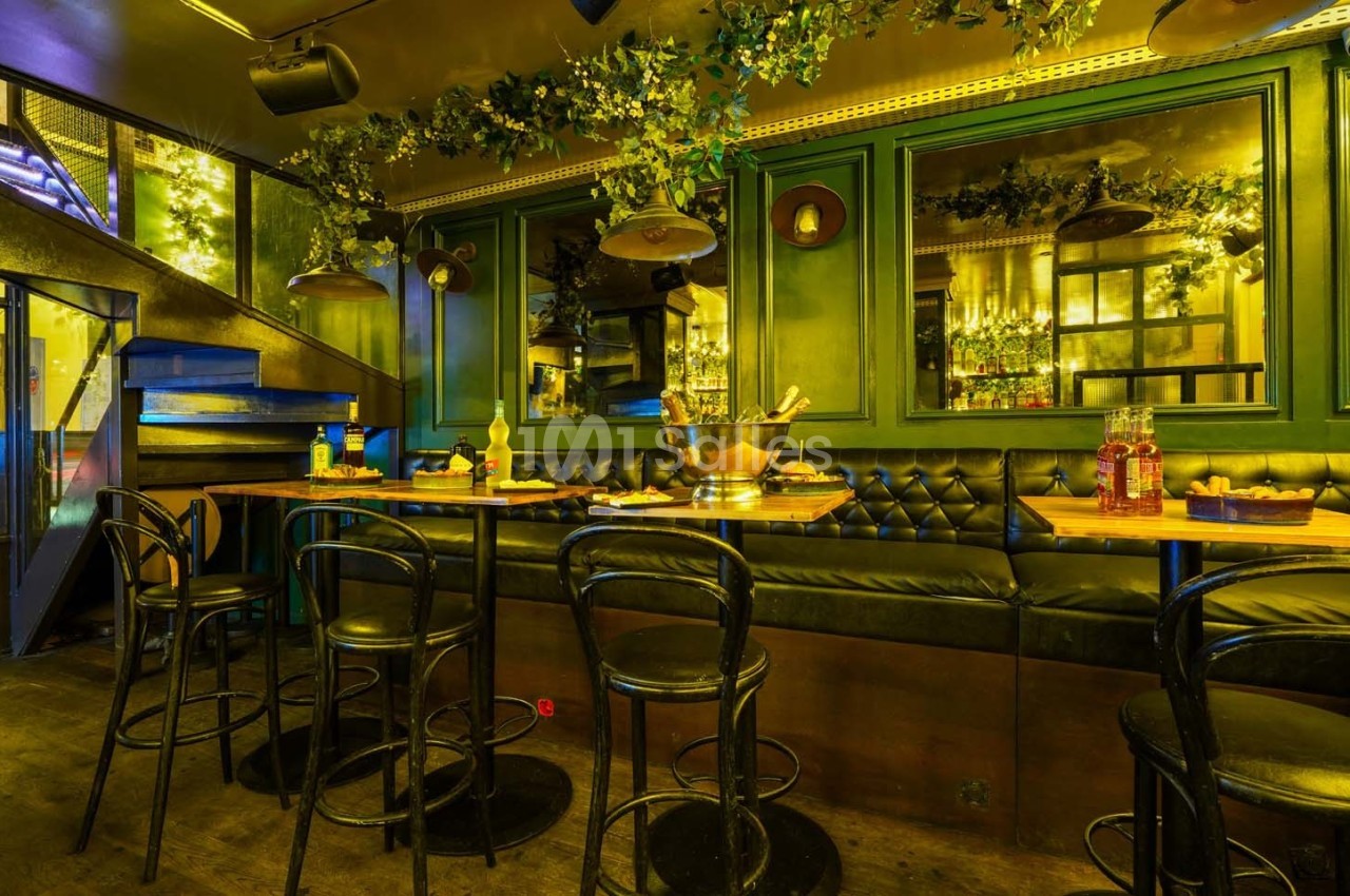 Salle de restaurant avec banquettes noires, tables en bois, chaises noires et décoration végétale suspendue.