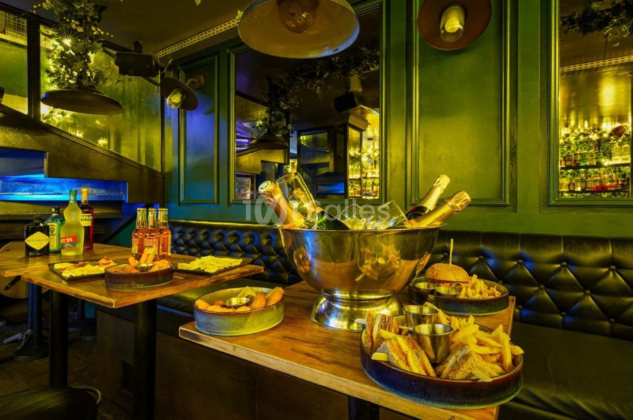 Salle de restaurant avec banquettes vertes, tables en bois garnies de plats variés et seau à champagne au centre.