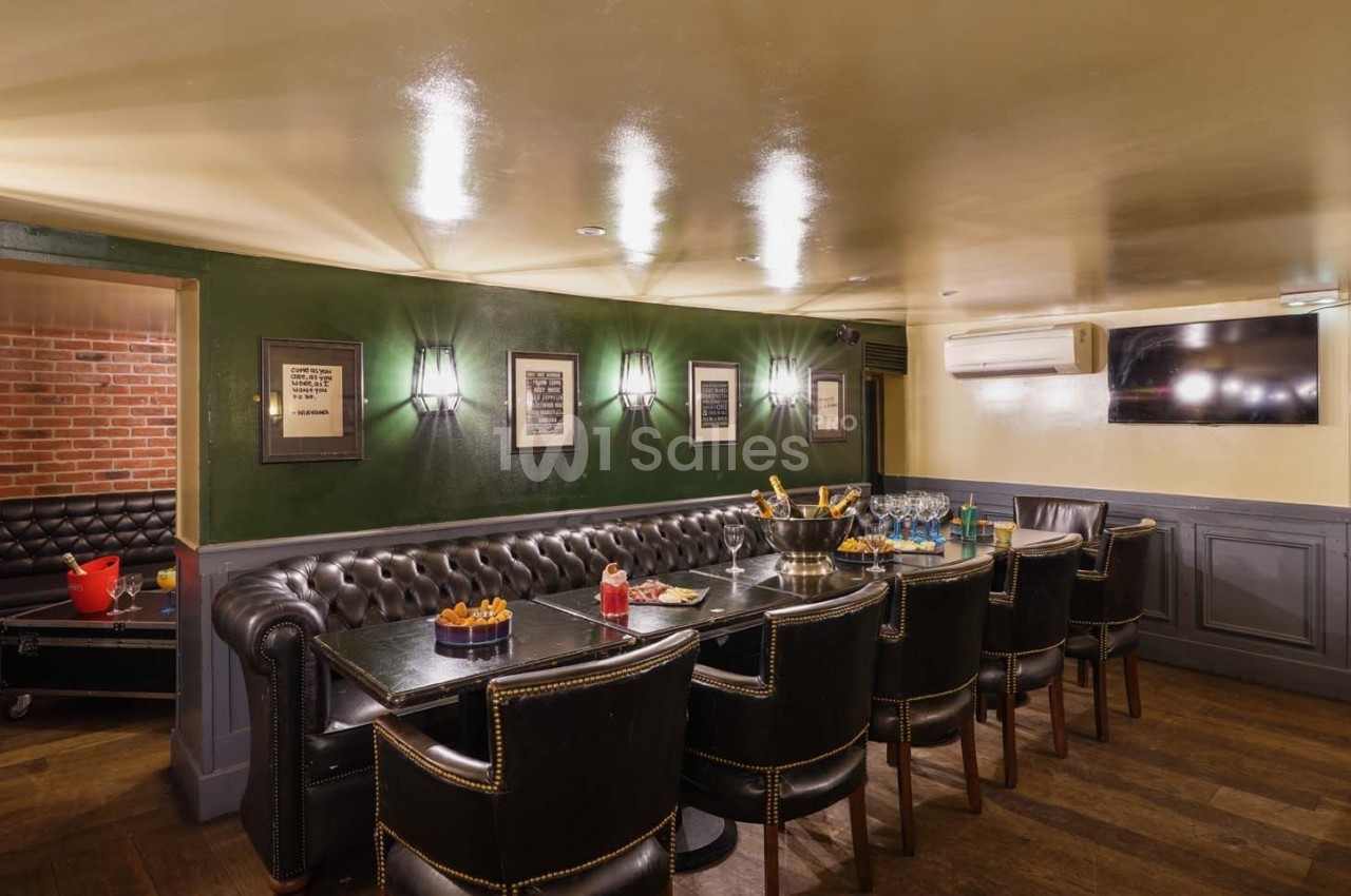 Salle à manger avec table en bois, chaises en cuir, murs verts décorés de cadres et éclairage tamisé.