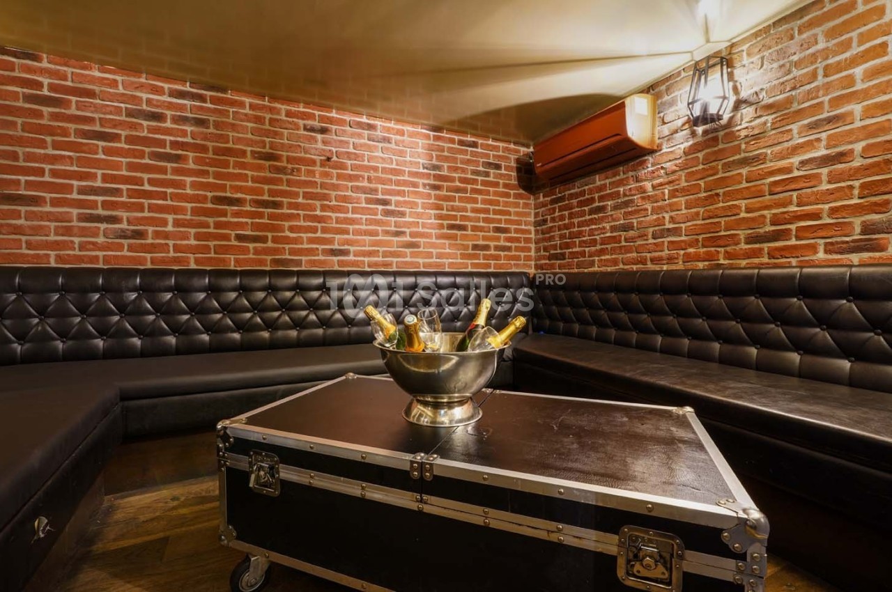 Salle avec murs en briques, banquettes en cuir noir et table basse avec un seau contenant des bouteilles de champagne.