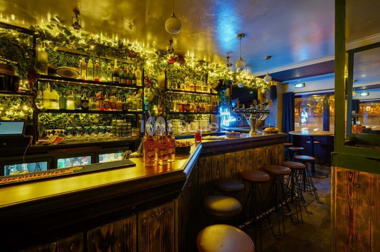 Intérieur d'un bar chaleureux avec comptoir en bois, étagères garnies de bouteilles et éclairage tamisé.