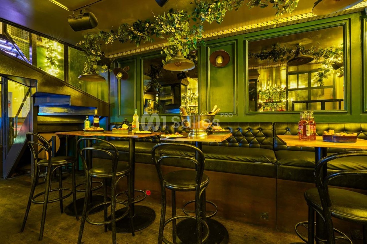 Salle de restaurant avec banquettes noires, tables en bois, chaises sombres et décorations végétales suspendues.