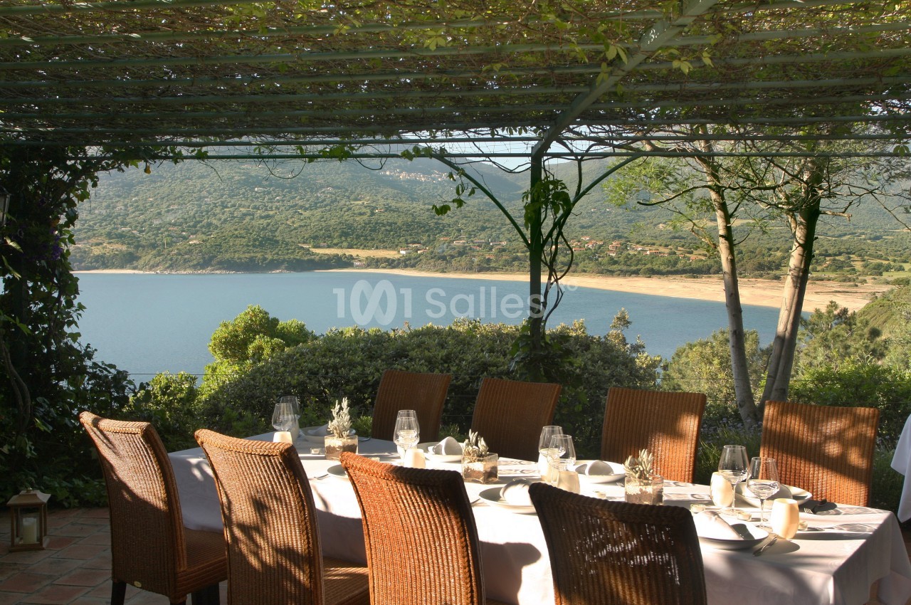 Table dressée sous une pergola ombragée avec vue sur un lac entouré de collines verdoyantes.