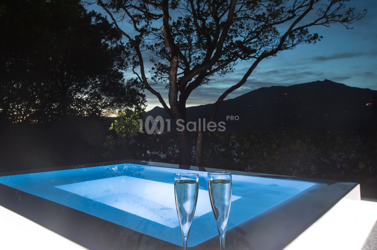 Bain à remous éclairé en extérieur, entouré d'arbres, avec deux verres de champagne au premier plan.