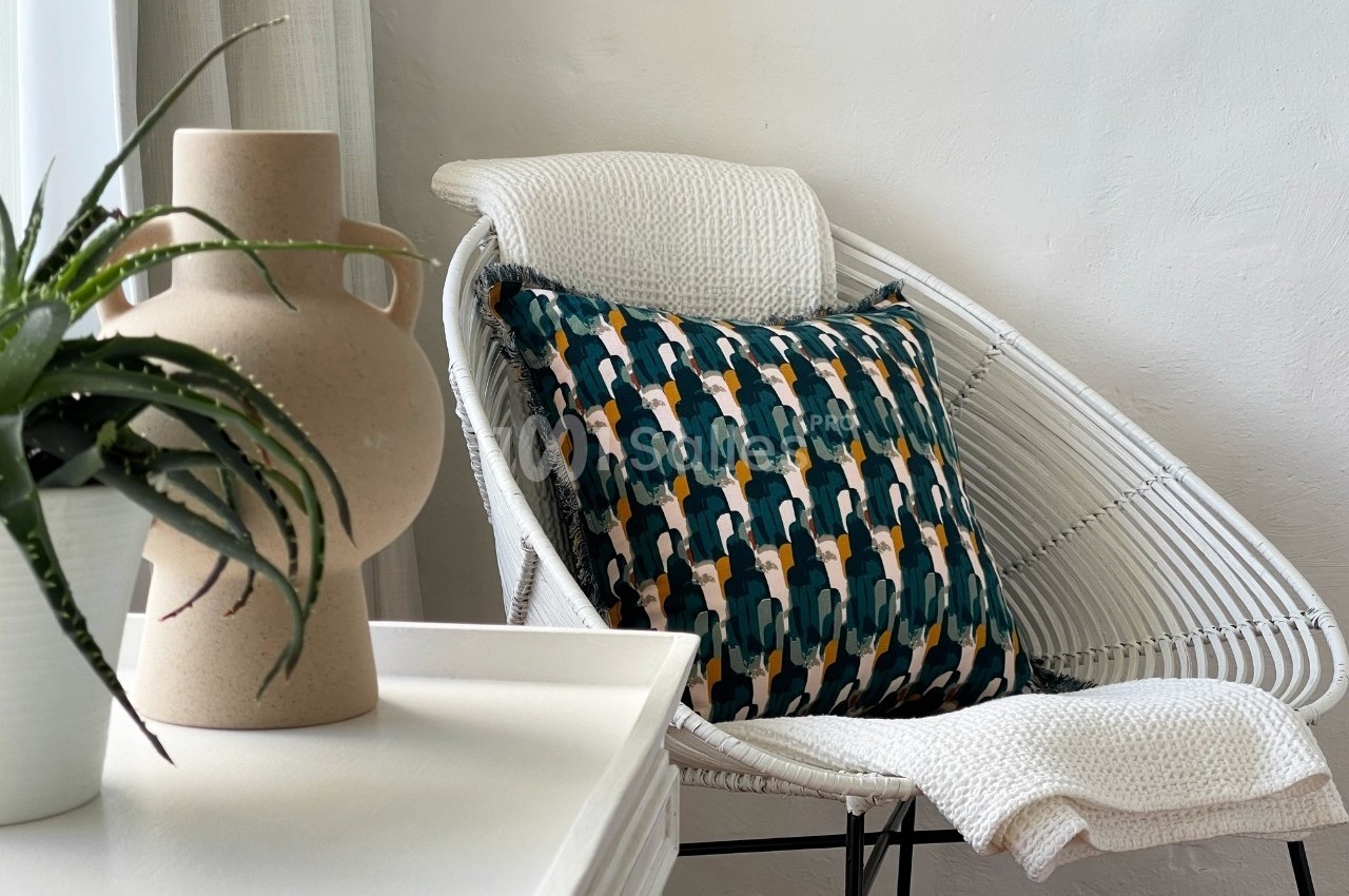 Fauteuil en rotin blanc avec un coussin à motifs géométriques colorés, près d'une table et d'une plante en pot.