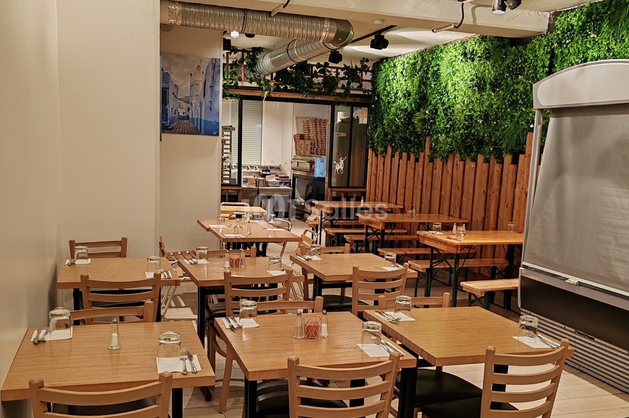 Salle de restaurant lumineuse avec tables en bois, chaises assorties et mur végétalisé en arrière-plan.
