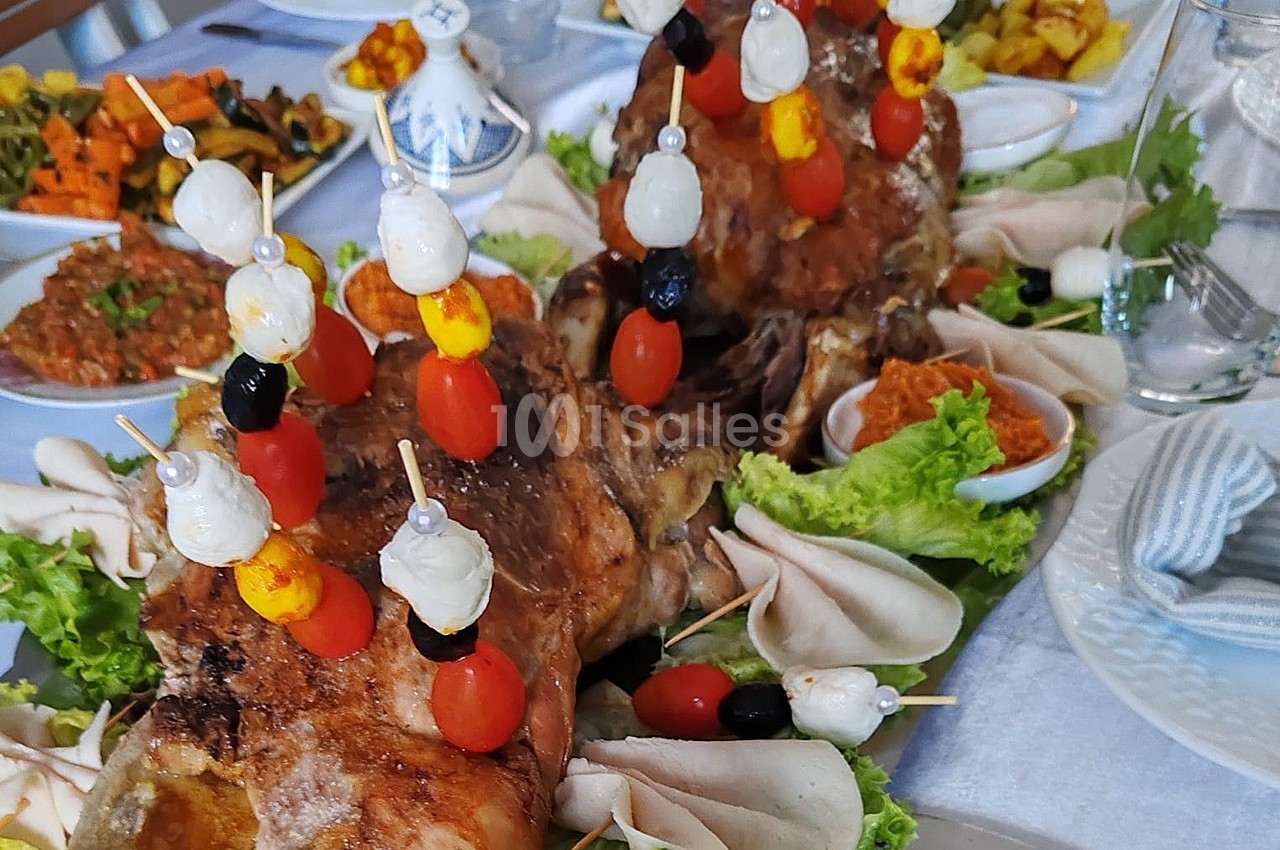 Plat de viande rôtie décorée de brochettes de légumes et servi avec des accompagnements variés sur une table dressée.
